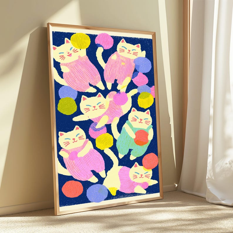 May include: A framed vertical art print featuring a dark blue background with multiple cream-colored cats wearing pink or light green overalls. The cats are depicted playing with various colorful yarn balls in shades of yellow, pink, blue, and orange.