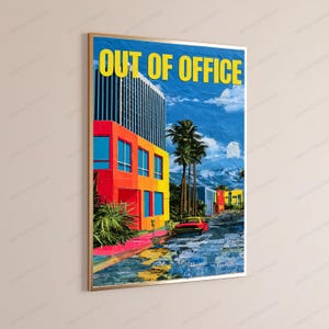 May include: A framed wall art print featuring a vibrant urban scene with a tall building in shades of orange, yellow, and blue. The text OUT OF OFFICE is printed in yellow at the top. A red car sits on a street with palm trees and mountains.