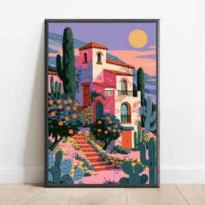 May include: A framed art print featuring a pink Mediterranean-style villa with a terracotta roof, surrounded by orange trees and tall green cacti. A stone staircase leads to the entrance under a yellow sun in a purple sky with distant blue mountains.