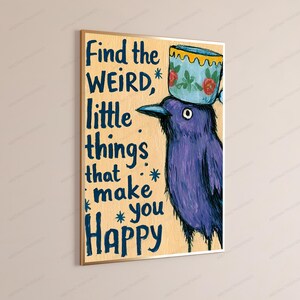 Op de afbeelding: Een rechthoekige wandkunstprint op een lichtbruine achtergrond met een paarse vogel met een blauw-wit theekopje op zijn kop. De tekst luidt: Find the WEIRD, little things that make you Happy. De vogel heeft een donkere snavel en oog.