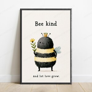 K&ouml;nnte beinhalten: Ein gerahmter Kunstdruck mit einer flauschigen, runden Hummel mit schwarzen und gelben Streifen, die einen kleinen braunen Topf auf dem Kopf tr&auml;gt und eine gelbe Blume h&auml;lt, mit dem Text Bee kind and let love grow in schwarzer Schrift.