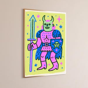 May include: A framed wall art print featuring a cartoon warrior with horns, a pink body, and blue armor. The figure holds a tall blue sword and a blue shield with a green skull emblem. The background is light green with scattered blue and pink stars.