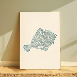May include: A rectangular framed wall art print featuring a centered, textured blue illustration of a flatfish on a solid off-white background. The fish is depicted in profile with a detailed, mottled ink-stamped appearance and a thin frame.