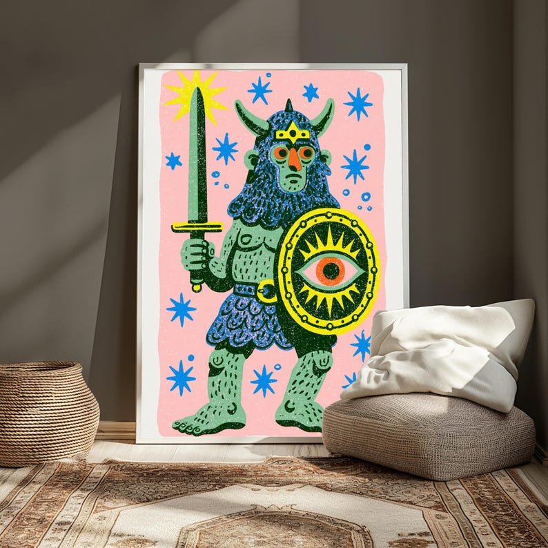 May include: A framed art print featuring a green, horned warrior figure on a pink background. The figure holds a grey sword and a yellow shield with a central eye motif. Blue star shapes are scattered across the pink field, and the warrior wears a textured blue tunic and helmet.