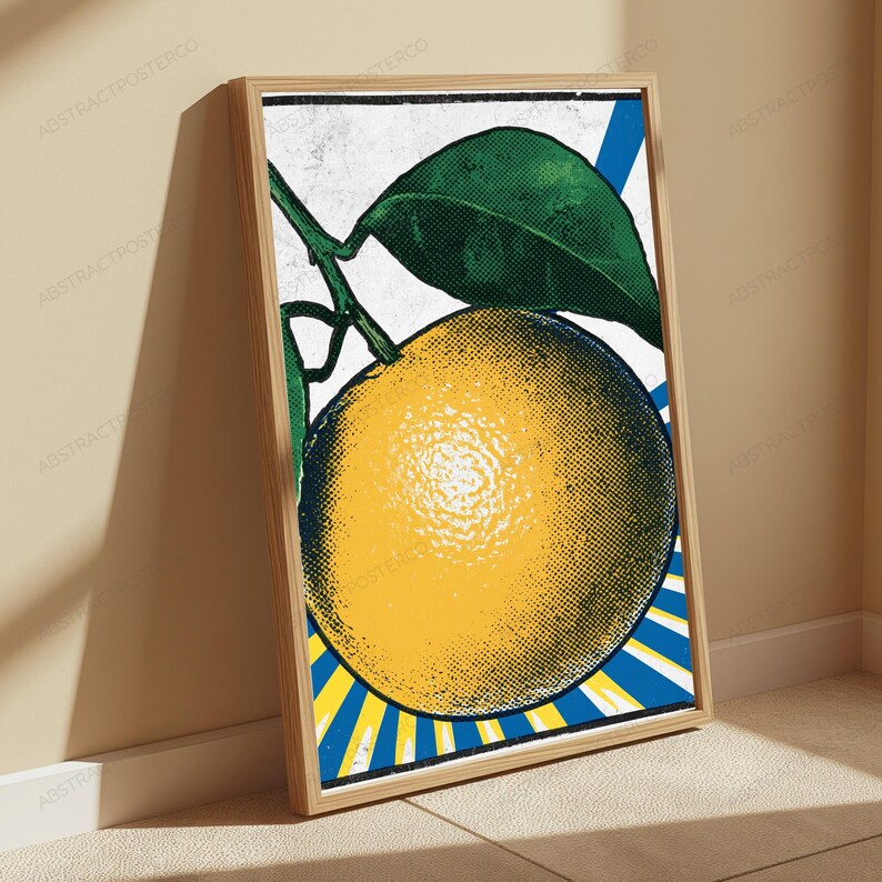 May include: A framed wall art print featuring a pop art style illustration of a yellow orange with green leaves. The background consists of blue and white radiating sunburst lines. The artwork has a textured, halftone dot pattern throughout.