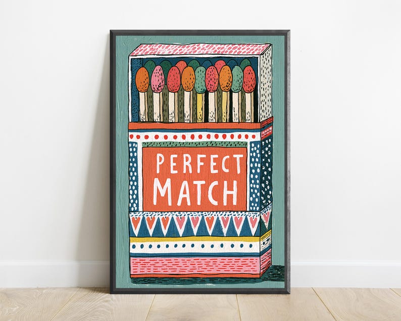 Op de afbeelding: Een ingelijste kunstdruk met een gestileerde illustratie van een open luciferdoosje gevuld met kleurrijke lucifers. Het centrale oranje rechthoekige paneel toont de witte tekst PERFECT MATCH. Het doosje is versierd met geometrische patronen in blauw, roze en geel.
