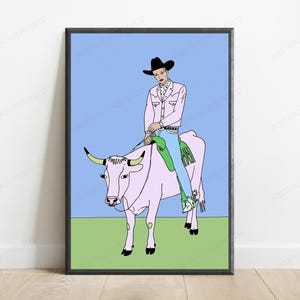 May include: A framed wall art print featuring a line-art illustration of a person wearing a black cowboy hat, a light pink jacket, and blue jeans, riding a light pink cow against a light blue sky and a solid light green ground.