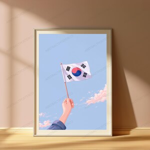 May include: A framed art print featuring an illustration of a hand holding a South Korean flag against a light blue sky with soft pink clouds. The flag displays a white background with a central red and blue taegeuk and four black trigrams.