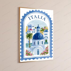K&ouml;nnte beinhalten: Ein gerahmter Kunstdruck mit einer Aquarellillustration eines Geb&auml;udes im mediterranen Stil mit blauer Kuppel, einer Palme und rosa Blumen, eingefasst in einen blauen Briefmarkenrand mit dem Wort ITALIA am oberen Rand.
