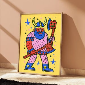 K&ouml;nnte beinhalten: Ein gerahmter Kunstdruck auf gelbem Hintergrund zeigt einen Cartoon-Wikinger mit blauem Bart und geh&ouml;rntem Helm. Die Figur tr&auml;gt eine rosa Tunika und blaue Stiefel und h&auml;lt eine rote Axt mit einem Gesicht auf der Klinge. Kleine blaue und rosa Sterne umgeben die Figur.