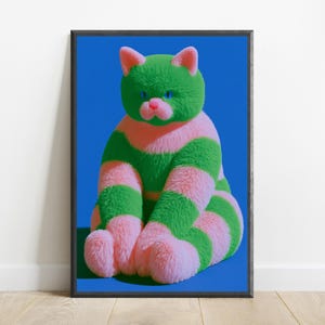 May include: A framed wall art print featuring a plush, fuzzy cat with horizontal stripes of bright green and soft pink. The cat has a pink nose, blue eyes, and pointed ears, set against a solid, vibrant blue background within a dark frame.