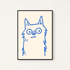 May include: A framed wall art print featuring a simple, hand-drawn illustration of a cat. The cat is rendered in a bold, bright blue line art style against a solid, light cream-colored background. The cat has large, wide eyes and pointed ears.