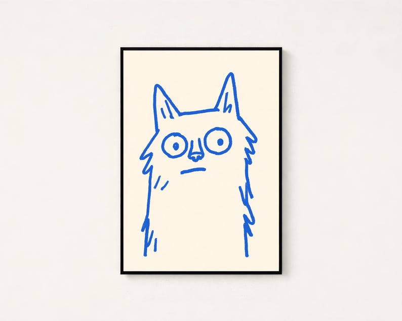 May include: A framed wall art print featuring a simple, hand-drawn illustration of a cat. The cat is rendered in a bold, bright blue line art style against a solid, light cream-colored background. The cat has large, wide eyes and pointed ears.