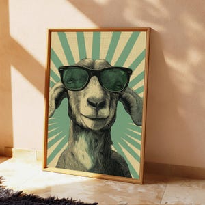 May include: A framed wall art print featuring a detailed illustration of a goat wearing black-rimmed sunglasses. The background consists of a light green and cream-coloured sunburst pattern with a subtle dotted texture throughout the design.