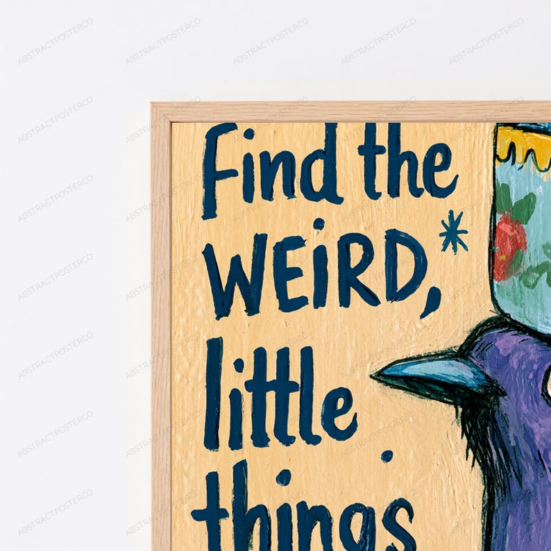 Op de afbeelding: Een ingelijste muurkunstprint met een lichtgele achtergrond en donkerblauwe handgeschreven tekst die Find the WEIRD, little things leest. Een deel van een paarse vogelillustratie met een kopje met bloemenpatroon op het hoofd is zichtbaar.