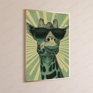 May include: A framed wall art print featuring a stylized illustration of a giraffe wearing black sunglasses. The giraffe is rendered in shades of green and black against a background of radiating light green and cream-colored sunburst rays.