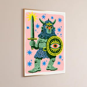 May include: A framed wall art print featuring a horned, blue-skinned warrior figure on a pink background. The figure holds a dark green sword and a round shield with a central eye motif. The scene is decorated with bright blue stars and a yellow sun.