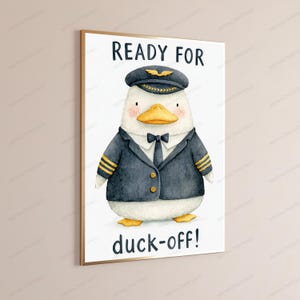 May include: A framed wall art print featuring a watercolor illustration of a white duck dressed as a pilot in a dark blue uniform with gold stripes, a tie, and a cap. The text reads READY FOR at the top and duck-off! at the bottom.