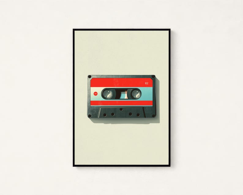 May include: A framed wall art print featuring a centered cassette tape with a red top section, a light blue middle band, and a dark gray bottom housing. The number 62 is printed in white on the top right, and a small red circle is on the left.