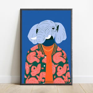 May include: A framed wall art print featuring an illustration of an elephant head with light blue skin and white tusks. The elephant wears an orange sweater under a dark green bomber jacket with a pink abstract pattern against a blue background.