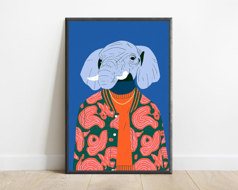 May include: A framed wall art print featuring an illustration of an elephant head with light blue skin and white tusks. The elephant wears an orange sweater under a dark green bomber jacket with a pink abstract pattern against a blue background.