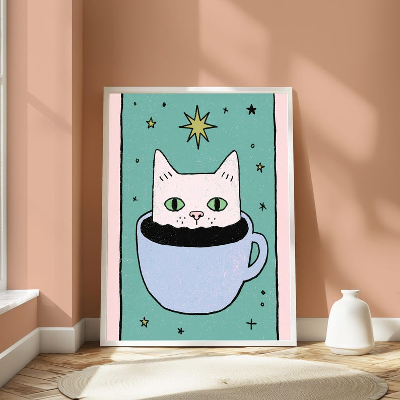 May include: A framed art print featuring a light pink cat with green eyes peeking out of a light blue coffee cup filled with black liquid. The background is a teal rectangle with small yellow stars and a large yellow star above the cat's head.