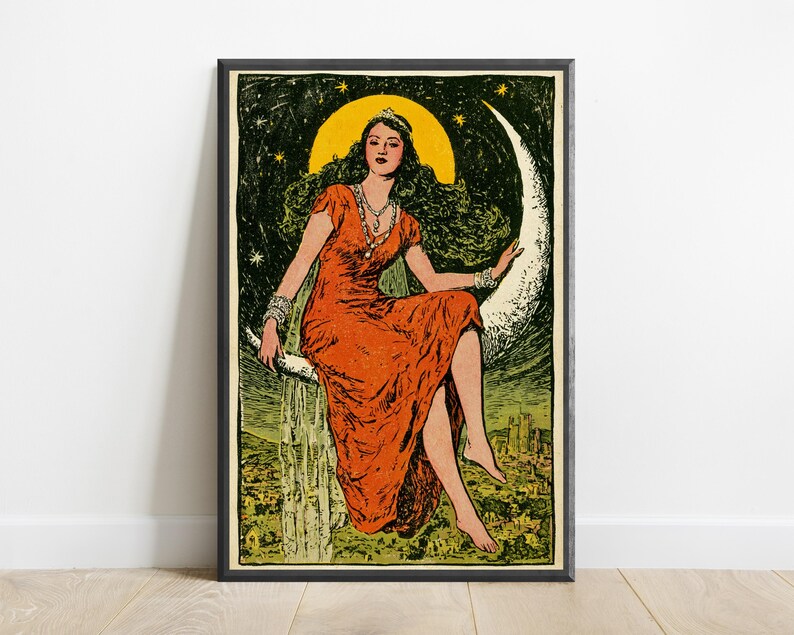 May include: A framed art print featuring a person with long dark hair wearing a vibrant orange dress and a tiara, sitting on a large white crescent moon against a dark green starry sky. Below the moon, a landscape with buildings is visible.