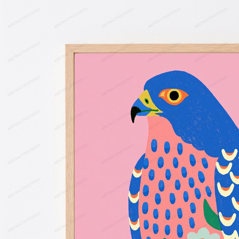 May include: A framed wall art print featuring a stylized blue falcon against a solid pink background. The bird has a bright yellow beak, a black eye, and a chest patterned with blue oval spots. The wings display blue and cream crescent shapes.