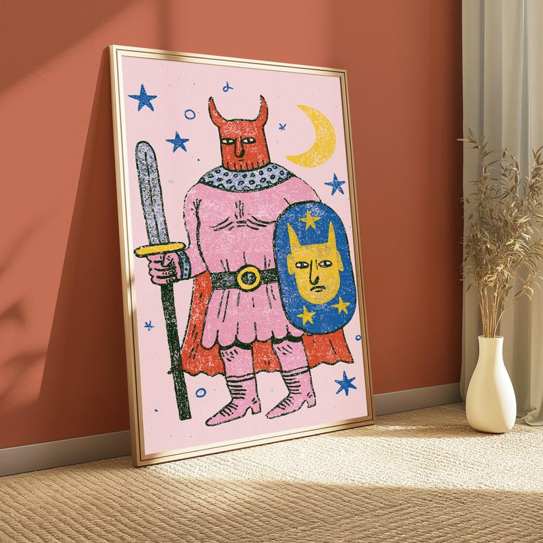 K&ouml;nnte beinhalten: Ein gerahmter Kunstdruck auf hellrosa Hintergrund zeigt eine rote geh&ouml;rnte Figur in einer rosa Tunika und einem Umhang, die ein dunkelgraues Schwert und einen blauen Schild mit einem gelben Gesicht und Sternen h&auml;lt. Das Bild enth&auml;lt einen gelben Mond.