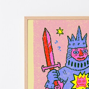May include: A framed art print featuring a stylized illustration of a knight in blue armor holding a red sword. The knight wears a blue crown and has a pink face. A yellow star and a small yellow sun-like icon with a face are visible on the pink background.