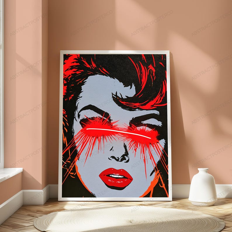 May include: A rectangular wall art print featuring a stylized graphic illustration of a face with grey skin, dark hair, and bright red lips. A horizontal white line crosses the eyes, with vibrant red light rays emanating outward from the eye area.