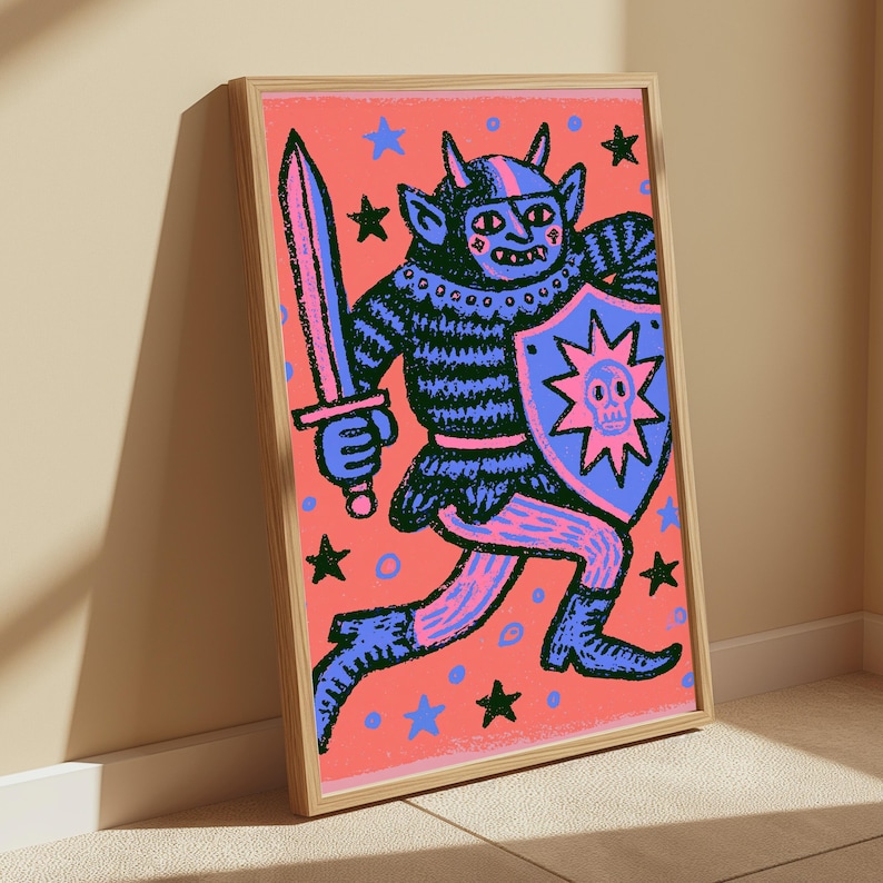 May include: A framed art print featuring a dark blue horned creature in armor holding a sword and a shield with a skull emblem. The background is a vibrant coral pink filled with scattered blue and black stars and small circles in a bold graphic style.