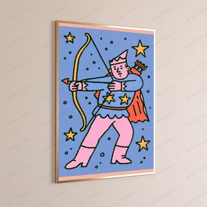 May include: A framed wall art print featuring a stylized illustration of a figure in a crown and cape holding a yellow bow and arrow. The character wears a blue top with yellow stars and pink pants against a blue background with yellow stars.