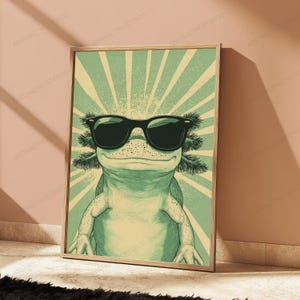 May include: A framed wall art print featuring a light green axolotl wearing black sunglasses. The background consists of a pale yellow and green sunburst pattern radiating from behind the axolotl, creating a graphic illustration style.