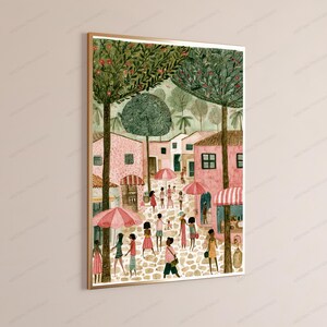 May include: A framed vertical wall art print depicting a Mediterranean-style town square with pink buildings, cobblestone paths, and tall green trees. Several figures walk through the scene carrying pink umbrellas under a soft, light-filled sky.