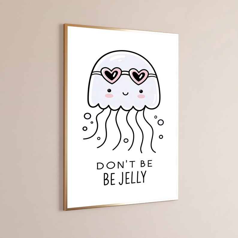 May include: A framed wall art print featuring a white cartoon jellyfish wearing pink heart-shaped sunglasses. The jellyfish has a smiling face with pink cheeks and wavy tentacles. Below the illustration, the text reads DON'T BE BE JELLY.