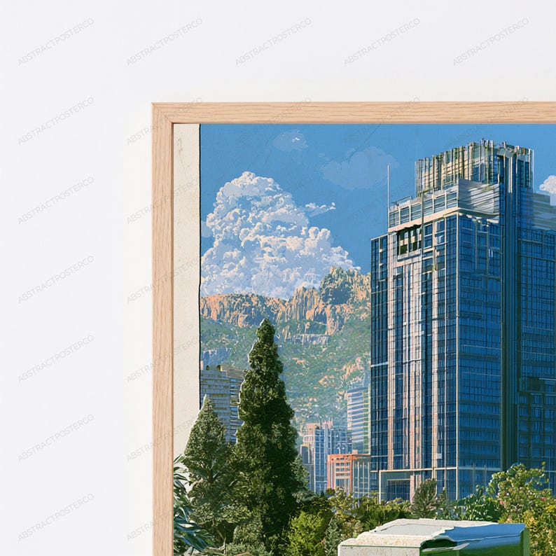 May include: A framed wall art print featuring a tall blue glass skyscraper set against a backdrop of rugged mountains and a bright blue sky with white clouds. The foreground includes green trees and a light-colored wooden frame border.