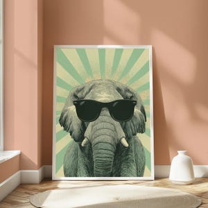 May include: A framed wall art print featuring a detailed illustration of an elephant wearing black sunglasses. The elephant is centred against a background of radiating light green and cream-coloured sunburst lines in a vintage pop art style.