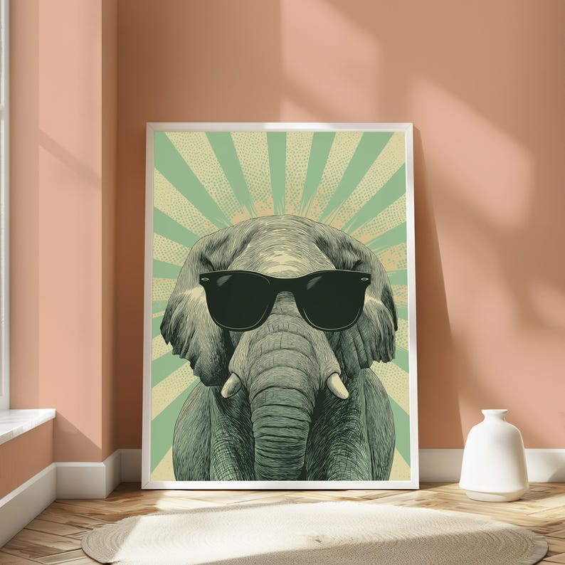 May include: A framed wall art print featuring a detailed illustration of an elephant wearing black sunglasses. The elephant is centred against a background of radiating light green and cream-coloured sunburst lines in a vintage pop art style.