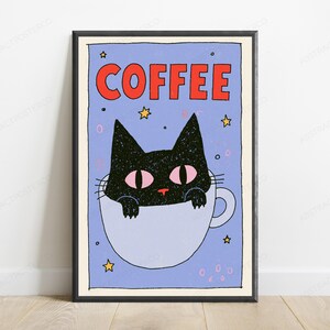 May include: A framed wall art print featuring a black cat with pink eyes sitting inside a light blue coffee mug. The background is light blue with yellow stars and small pink circles. The word COFFEE is printed in bold red letters at the top.
