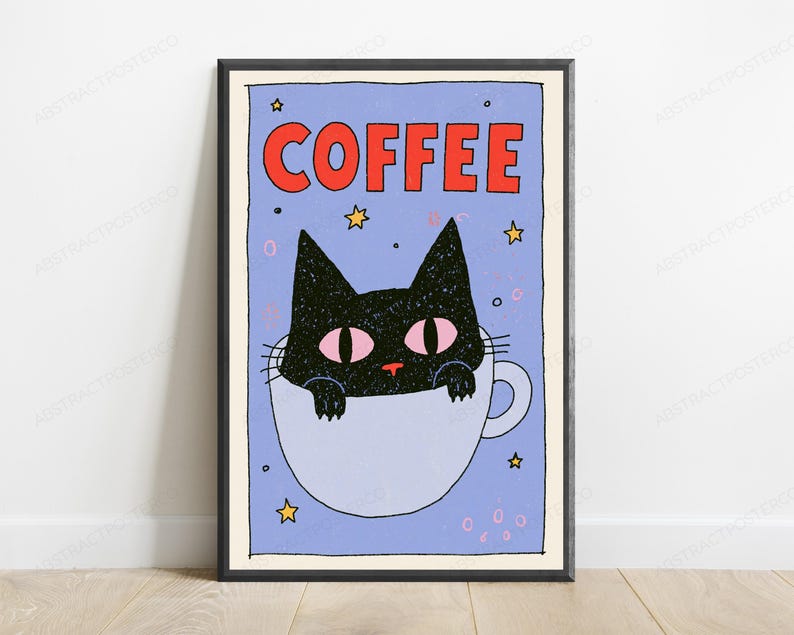 May include: A framed wall art print featuring a black cat with pink eyes sitting inside a light blue coffee mug. The background is light blue with yellow stars and small pink circles. The word COFFEE is printed in bold red letters at the top.