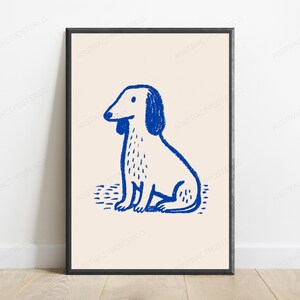 May include: A framed wall art print featuring a blue line drawing of a sitting dog on a light beige background. The dog illustration has a textured, hand-drawn appearance with simple features, including floppy ears and a small tail, set against a plain backdrop.