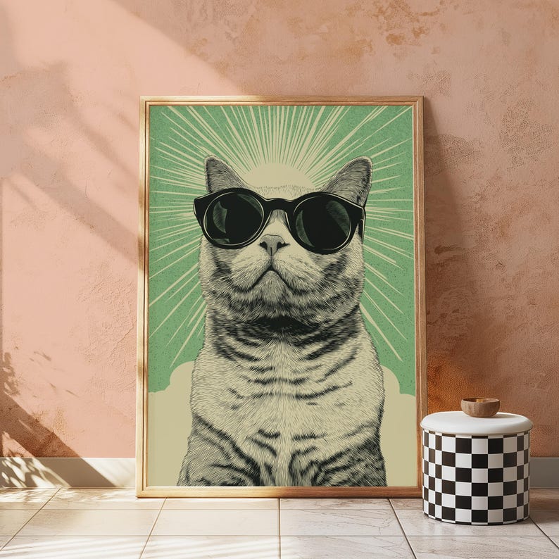 May include: A framed wall art print featuring a detailed illustration of a cat wearing large black sunglasses. The cat is centered against a light green background with radiating white sunburst lines and a cream-colored base area.