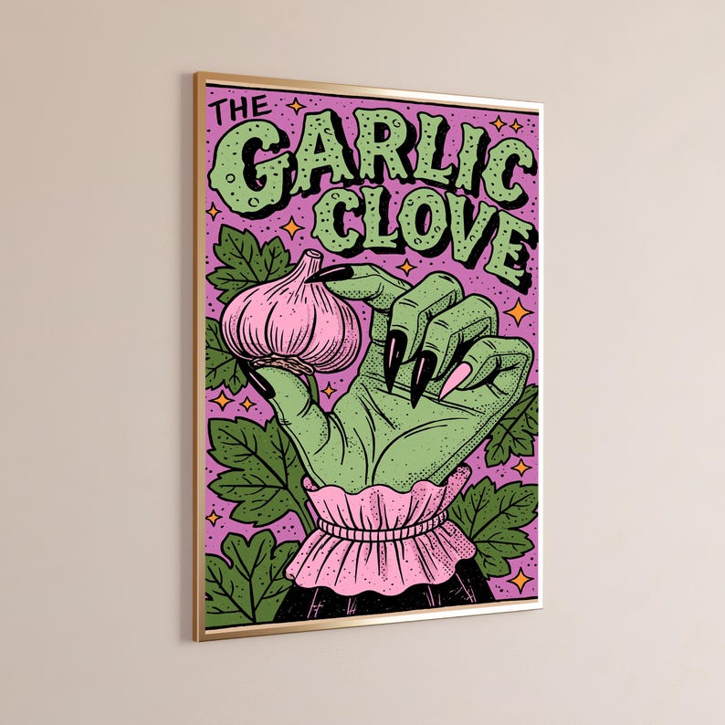 Pu&ograve; includere: Una stampa artistica da parete incorniciata raffigurante una mano verde con lunghe unghie nere che tiene un bulbo d'aglio rosa su uno sfondo viola con foglie verdi e stelle arancioni. Il testo THE GARLIC CLOVE &egrave; stampato in grandi lettere verdi.
