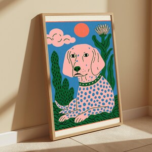 K&ouml;nnte beinhalten: Ein gerahmter, rechteckiger Wandkunstdruck, der einen rosa Hund mit blauen Punkten, einem gr&uuml;nen Halsband und einem gr&uuml;n gemusterten K&ouml;rper zeigt. Der Hintergrund umfasst einen blauen Himmel, eine rosa Wolke, eine orange Sonne und gr&uuml;ne Pflanzen in einem hellen Holzrahmen.