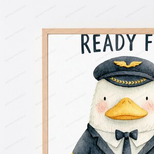 May include: A framed watercolor print featuring a white duck dressed as a pilot, wearing a dark blue captain's hat with gold wings and a black bowtie. The text READY F is visible at the top. The artwork is enclosed in a light wood frame.