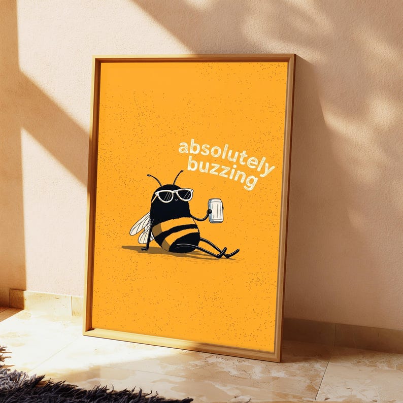 May include: A framed wall art print featuring a yellow background with a cartoon bee wearing white sunglasses and holding a silver can. The bee has black and yellow stripes and white wings. The text absolutely buzzing is printed in white.