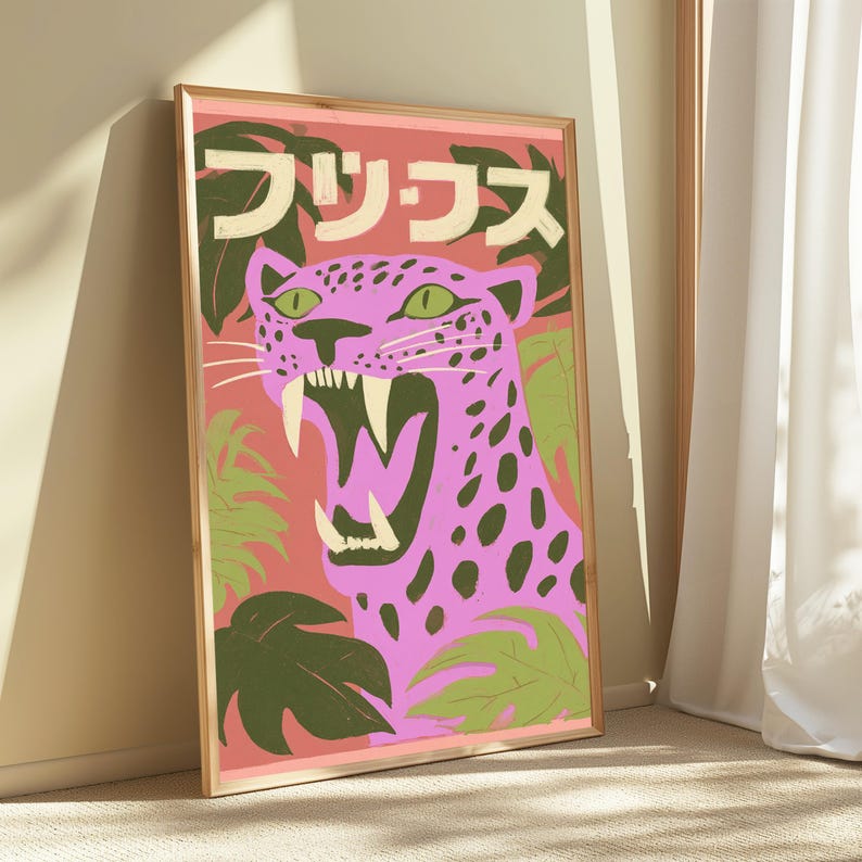 May include: A framed rectangular wall art print featuring a pink leopard with dark spots and an open mouth showing sharp teeth. The background is a salmon color with dark green tropical leaves and Japanese text at the top in cream-colored letters.