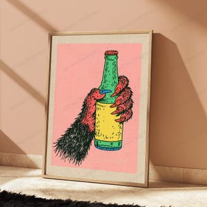 May include: A framed art print featuring a graphic illustration of a hairy, clawed creature hand holding a green glass bottle with a yellow label. The background is a solid light pink colour, and the creature's fur is rendered in black and red.
