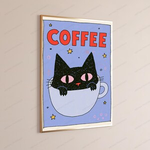 May include: A framed wall art print featuring a light blue background with the word COFFEE in bold red letters at the top. A black cat with pink eyes is illustrated peeking out from a white coffee mug, surrounded by small yellow stars.